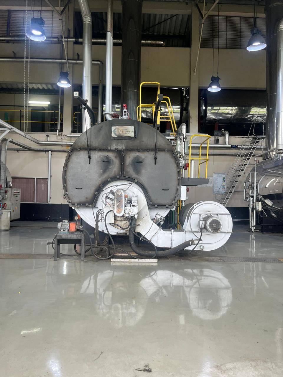 Front view of a large fire-tube boiler with its burner and fan in a clean industrial boiler house