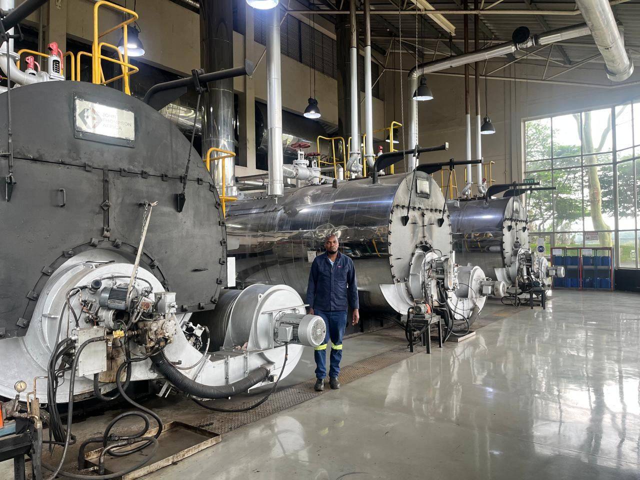 A Boiler Engineers technician standing beside a row of John Thompson package boilers in a client boiler house