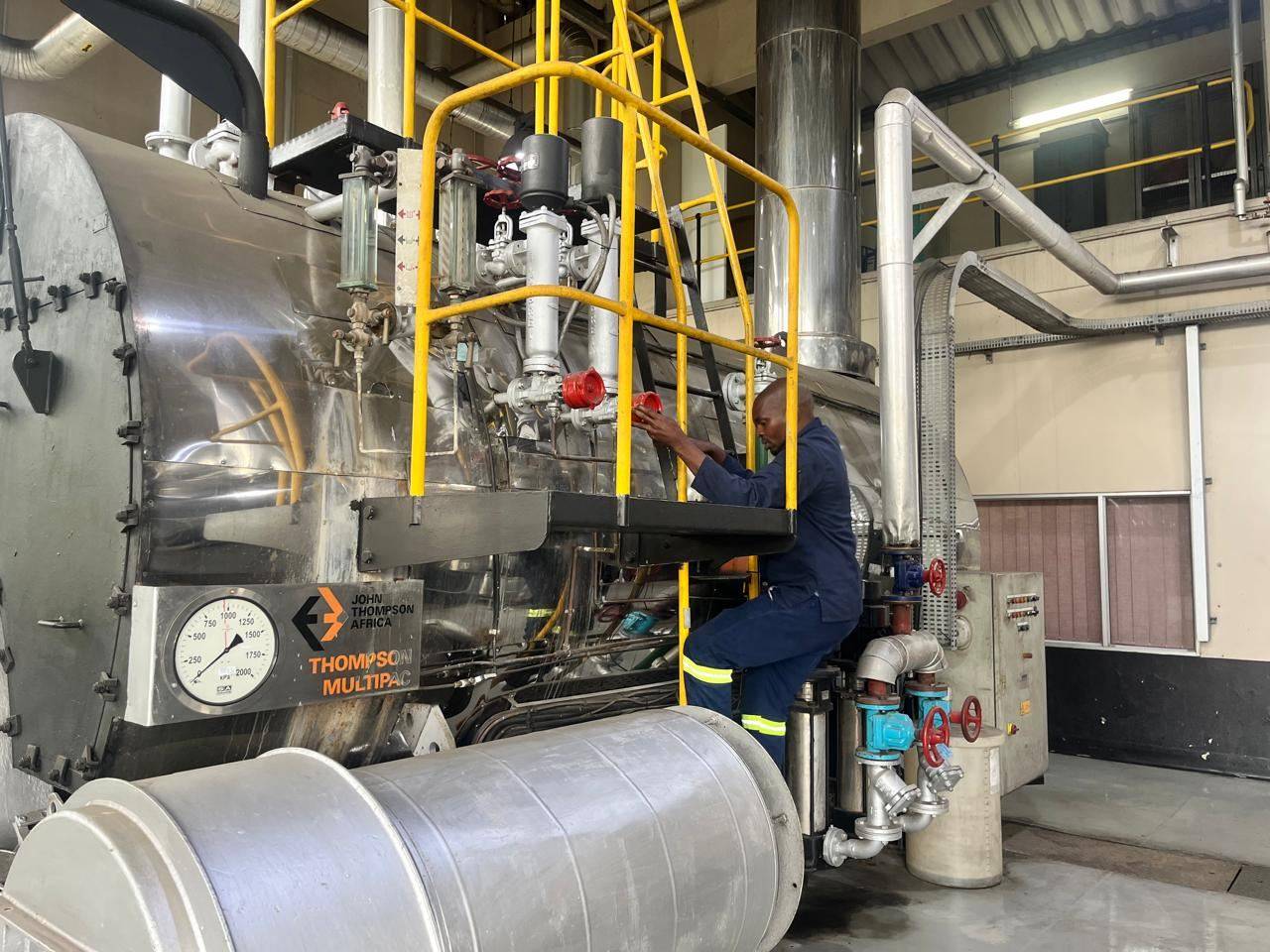 Technician operating valves on the gauge-glass and feed-water assembly of a package boiler